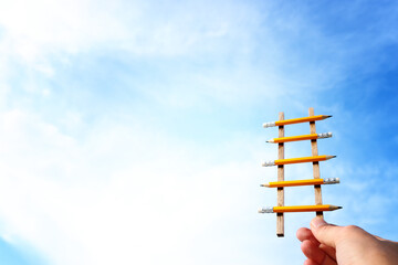 Concept image of a ladder made of pencils reaching the clouds. Idea of education, success and achieving goals