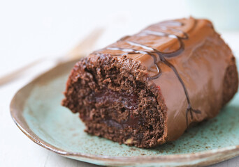 Chocolate roll cake in plate on white wooden background.