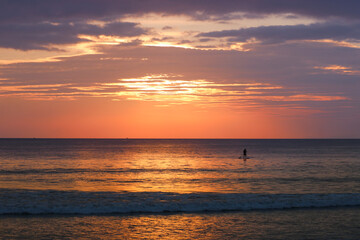 Silhouette of a man on a SUP board in the sea against the backdrop of a colorful sunset. Tropical island, vacation, active recreation at sea, travel.