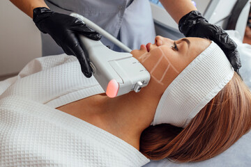 Portrait of relaxed young female client getting SMAS ultrasound face lifting massage