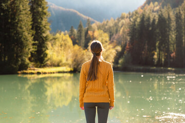 Young woman standing on a pier and enjoying the scenery. Adventure travel in Slovenia, mountain lake in Jezersko. Vibrant autumn colors on a sunny day in the Alps.
