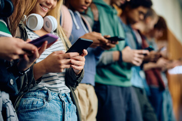 Close up of high school students using smart phones in hallway.