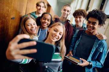 Multiracial group of happy students taking selfie at high school.