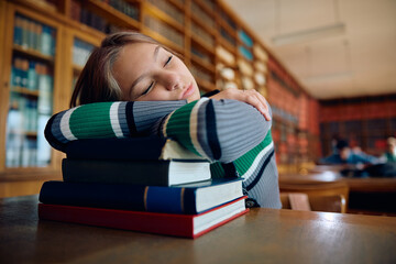 Tired high school student sleeping on books in library.