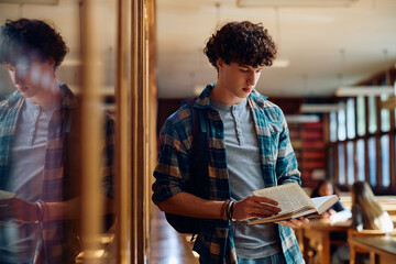 High school student learning from book in library.