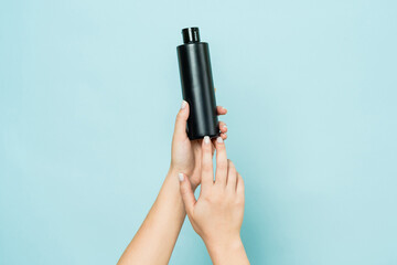 Hands hold black bottle of cosmetic product for skin on blue background - obrazy, fototapety, plakaty
