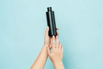 Foto op Plexiglas Hands hold black bottle of cosmetic product for skin on blue background © Anton Tolmachov