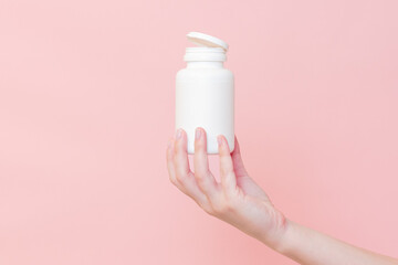 Blank white plastic tube in hand on pink background. Cosmetics beauty mockup for product branding