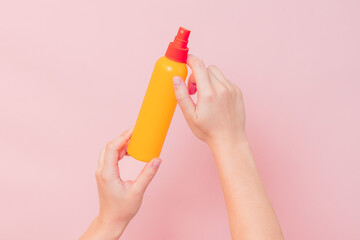 Hand holding plastic spray bottle (as mineral spray or hair spray) on pink background. Cosmetics...