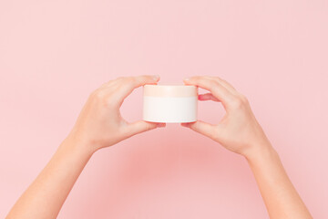 Fototapeta na wymiar Round jar of cosmetic cream in hand on pink background. Cosmetics beauty mockup for product branding