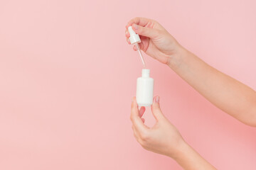 Hand holding glass cosmetic bottle for serum (hyaluronic acid and collagen) on pink background. Beauty concept