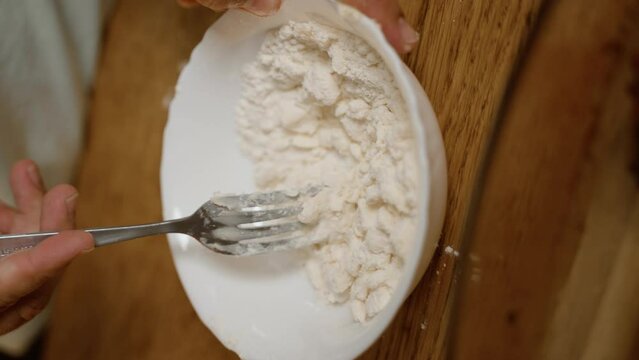 Hands using a fork to mix flour in a bowl, a close-up perfect for stock videos depicting the initial steps of baking or meal preparation, showcasing fundamental cooking techniques. 