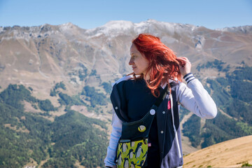 Red-haired girl in the mountains, hand at her head, in profile