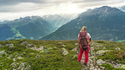 Ein Wanderin mit Rucksack auf der Alpenüberquerung blickt vom Venet ins Pitztal.