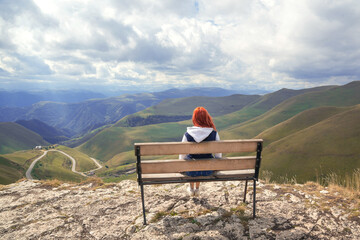 Girl sitting on the bench on a mountain hill, contemplating the beautiful mountainous view