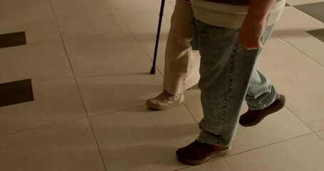 Mobility and independence of seniors. Elderly couple strolling with support of cane in sunny indoors. No face. Issues associated with aging. Aged couple walking together.