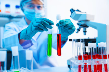 Asian people scientist in lab coat and protective gloves working with test tubes with green and red liquids, with microscope and other test tubes in the background in laboratory.