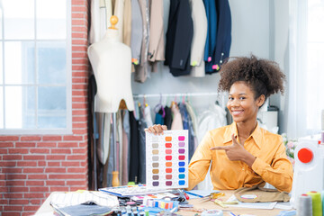 Young African American designer showing fabric sample, looking at cameraworking in fashion studio...