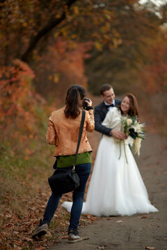 female wedding photographer taking pictures of the bride and groom on the wedding day in autumn