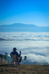 Asian Man is happy and relaxed with the scenery of the sea mist a beautiful natural in the morning at Car Camping site on the top of a mountain in winter season at Chiang Mai, Thailand.