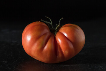 ripe raf tomato on black background, portrait in dark red