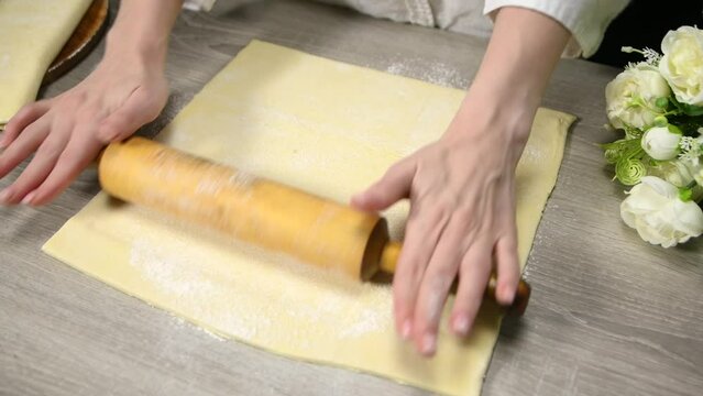 woman rolling out dough with a rolling pin on table in the kitchen