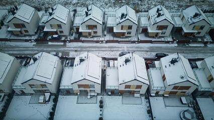 Aerial view of rows of identical houses covered in snow, with solar panels also covered by white snow on the roofs, on a cold and freezing day.