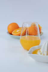 a glass glass with orange juice in the foreground, a plate with oranges in the background. White background