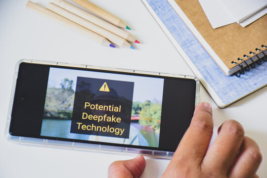 Smartphone screen displaying warning sign of using deepfake technology in an artificial image.