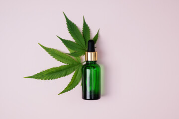 Cannabis oil and hemp leaf on pink background, flat lay. Hemp CBD oil in a bottle. Herbal cannabis...