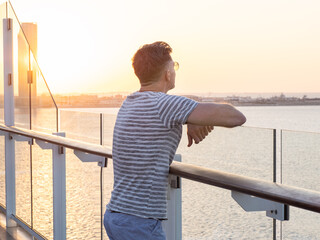 Handsome man standing on the empty deck of a cruise liner against the backdrop of sea waves. Sunny, clear day. Closeup, outdoor. Vacation and travel concept