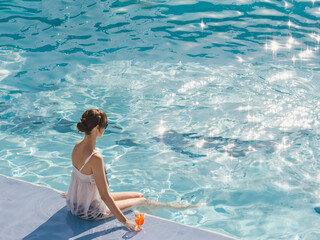 Cute woman with a glass of drink sits near the swimming pool of a cruise ship. Sunny, clear...