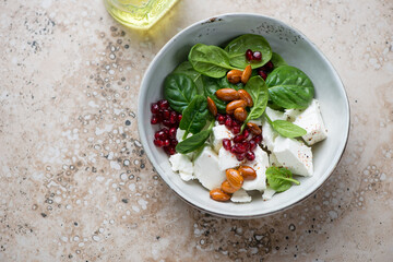 Grey bowl with feta cheese, baby spinach, pomegranate and almonds salad, horizontal shot on a beige granite background with space, high angle view