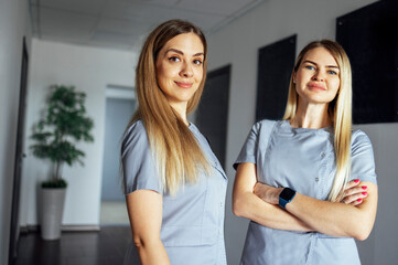 Beautiful smiling female doctors in medical uniform stands near the window in clinic
