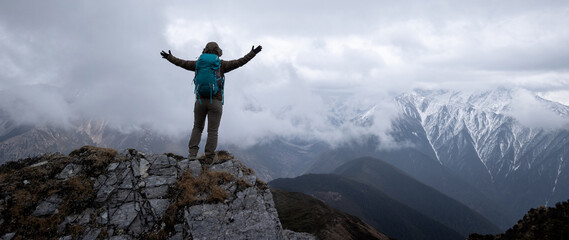 Woman hiker enjoy the view on mountain top cliff edge face the snow capped mountains in tibet - obrazy, fototapety, plakaty