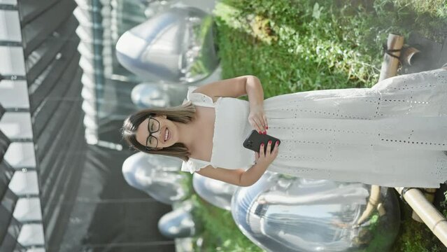 Beautiful hispanic woman with glasses, immersing in futuristic tech-art exhibition at a modern museum, capturing abstract objects on smartphone