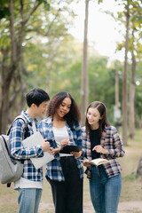 Three young college students is reading a book while relaxing sitting on grass in a campus park with her friends. Education concept