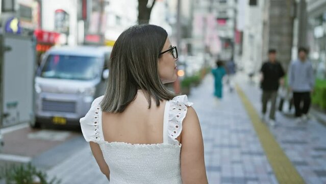 Back view of a beautiful hispanic woman walking away down tokyo street, looking at the urban surroundings through her glasses, capturing the city's life and architectural beauty