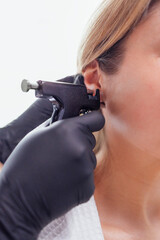 Close up of face of young blonde woman doing ear piercing procedure