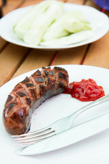 Barbequed Sausage served on a plate in a garden with ketchup and fresh cucumber - 704377300