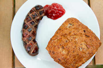 Barbequed Sausage served on a plate in a garden with ketchup and a roll - 704377314