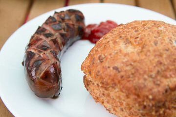 Barbequed Sausage served on a plate in a garden with ketchup and a roll - 704377315