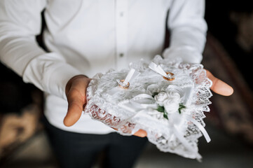 The groom holds a heart-shaped pillow with gold rings in his hands at the ceremony. Wedding...