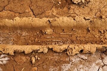 Trace of a car wheel on on the mud, soil land. Driving on desert sand after rain. Car tread pattern. Texture of a road with traces of car tires. Track, tracks. Footprint, Footprints