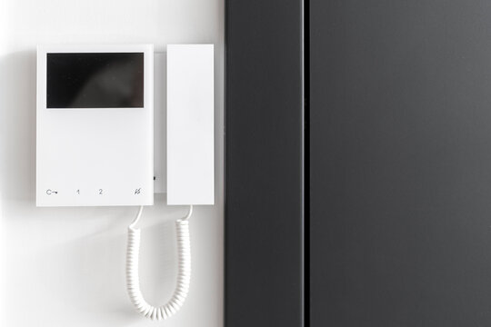 Close up view of electronic doorbell on white wall near black metal door