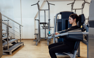Obraz premium Attractive brunette sportive woman doing exercises on the simulator in fitness club