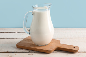 Jug with fresh milk on white wooden table