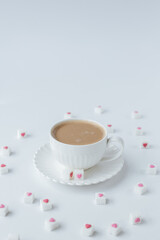 on a white background, a white cup with coffee, around refined sugar with hearts