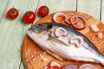 Board of raw dorado fish with vegetables on green wooden background