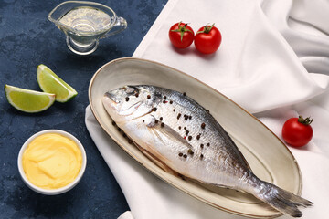 Plate of raw dorado fish with lime and sauce on blue background